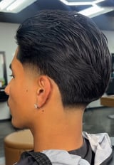 Side profile of man with modern black textured haircut, undercut fade, and ear piercing in salon setting
