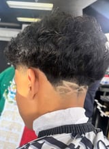 Back view of a man with a textured black curly hair fade haircut in a barber shop setting