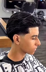 Side profile of a man with a sharp black pompadour hairstyle and faded undercut in a barbershop setting
