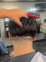 Person brushing the back of a mans freshly cut black hair with a red and gray brush at a barber shop