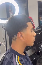 Profile view of a man with a short fade haircut in a salon with ring light visible in background