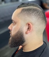 Man in profile wearing a fade haircut with thick beard, styled hair swept to the side