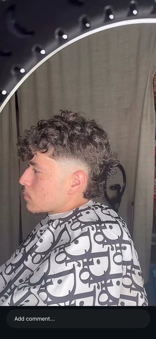 Man with curly hair fade haircut wearing patterned black and white shirt in front of vanity mirror with lights