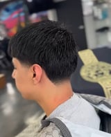Side view of person with short black hair and light skin tone wearing a light colored shirt in what appears to be an indoor setting