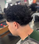 Back view of person with short black curly hair wearing green shirt in salon setting