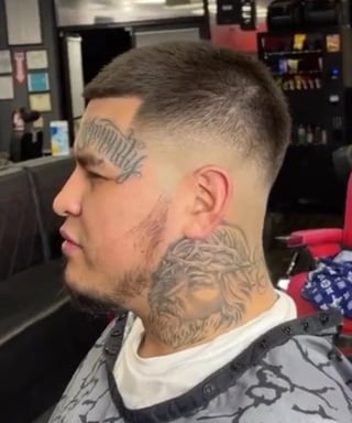 Man with short fade haircut and facial tattoos in profile view inside a barber shop