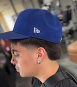 Person wearing a blue New Era baseball cap and black shirt, shown in profile view with pierced ear visible