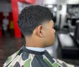 Side profile of a man with a short textured haircut, wearing a striped cape in a barbershop setting