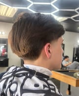 Person with short layered brown haircut viewed from behind in a modern barbershop with hexagonal ceiling lights