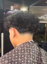 Back view of person with short dark curly hair wearing designer patterned shirt in indoor setting