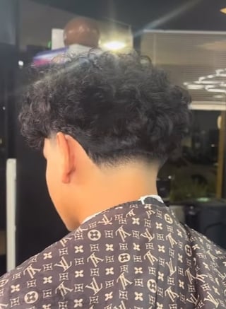 Back view of person with short dark curly hair wearing designer patterned shirt in indoor setting
