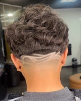 Back view of a mans short textured haircut with undercut fade and decorative line design on the nape