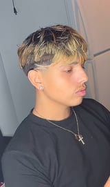Person with short blonde and dark two-tone textured hair, wearing black shirt and silver chain necklace, shown in profile view