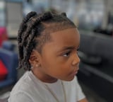 Child with braided hairstyle in profile wearing light-colored shirt, outdoor setting with blurred background