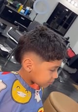 Young boy with a fresh fade haircut in a barbershop, wearing a blue cartoon character shirt