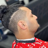 Side profile of man with man bun hairstyle, shaved sides, and facial hair wearing a red patterned shirt