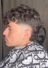 Side profile of a man with curly dark hair, fade haircut, and facial hair wearing a patterned black and white shirt