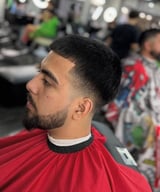 Man with beard and short dark hair in side profile at a barbershop, wearing a red cape
